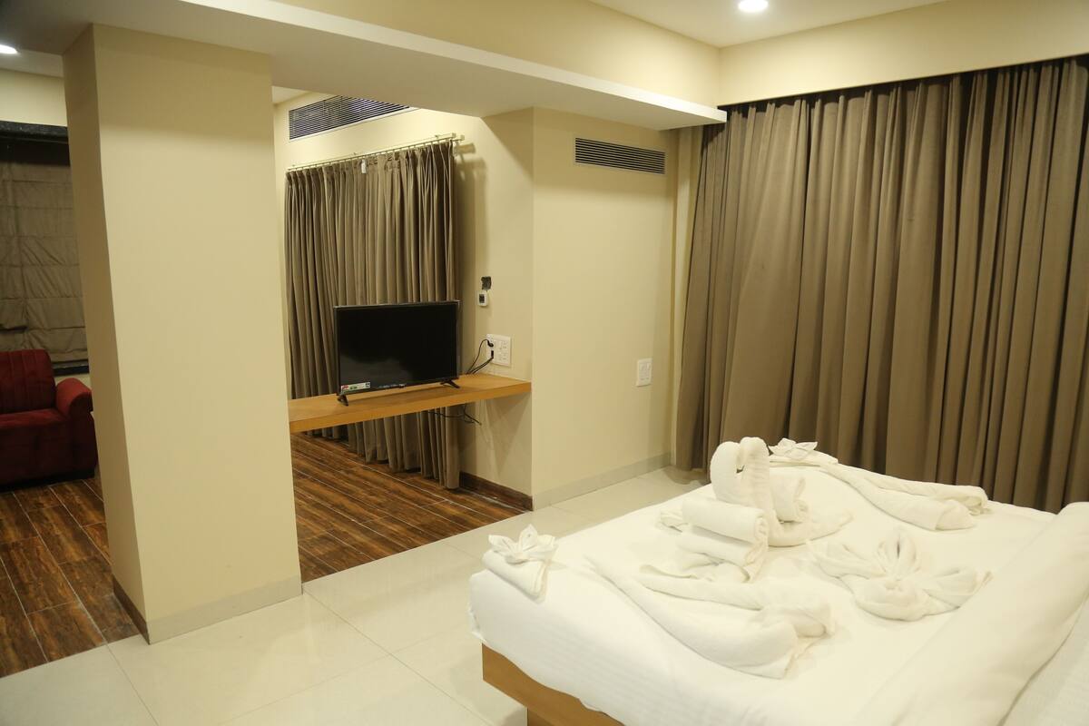 A hotel room with a bed, a TV on a wooden stand, and a red chair.