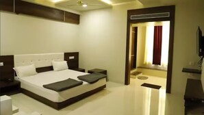 A modern hotel room with a large bed, bedside tables, a flat-screen TV, and a ceiling fan. - Mann Holiday Resort (Burhanpur)