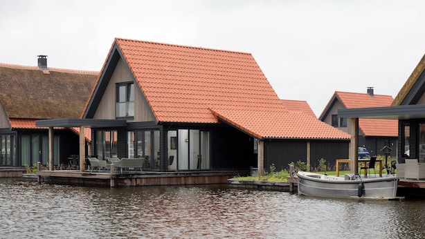 Una hilera de casas modernas con techos rojos, terrazas de madera y grandes ventanales con vista al agua.