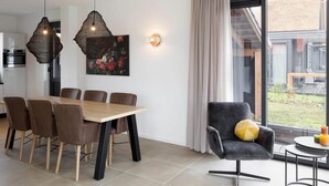 Un comedor moderno con una mesa y sillas de madera, un sillón negro con un cojín amarillo y una lámpara colgante.