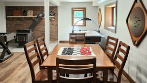 A dining area with a wooden table and chairs, a chessboard, and a brick wall with a fireplace.