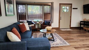 A living room with a blue sofa, two armchairs, a coffee table with a flower arrangement, a wooden floor, and a door with a window.