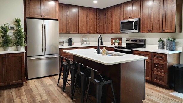 A modern kitchen with wooden cabinets, stainless steel appliances, and a central island with bar stools.