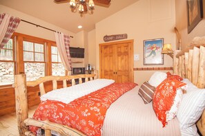 A bedroom with a wooden bed, a sign reading "Camp Hale", a television, and a window with curtains.