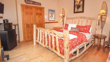 A wooden bed with red bedding, a wooden nightstand, a lamp, and a sign that reads "Camp + Hale".