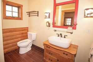 A bathroom with a wooden vanity, a white sink, a mirror, and a toilet.