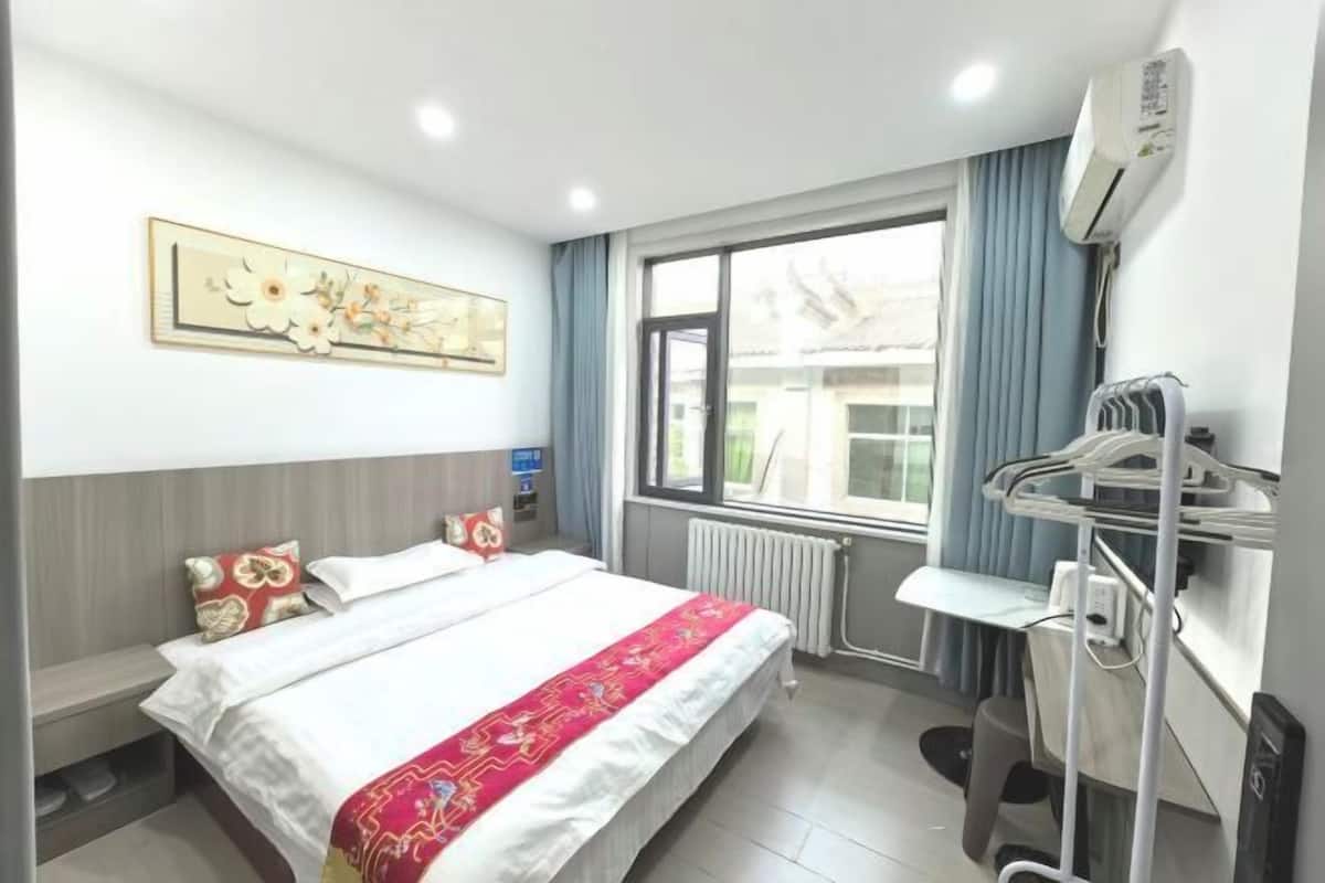 A hotel room with a bed, a window with curtains, an air conditioning unit, and a dental chair.
