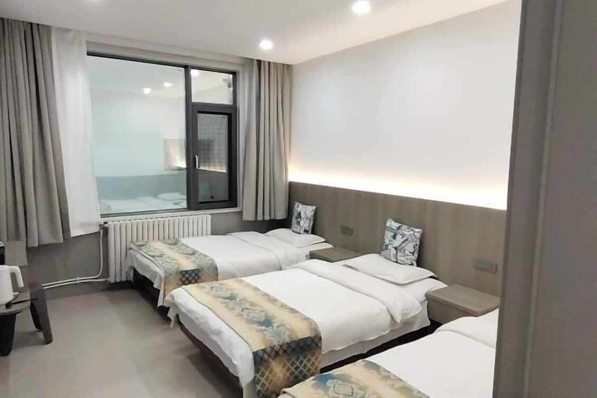 A hotel room with two beds, a window, a radiator, a desk, and a chair.