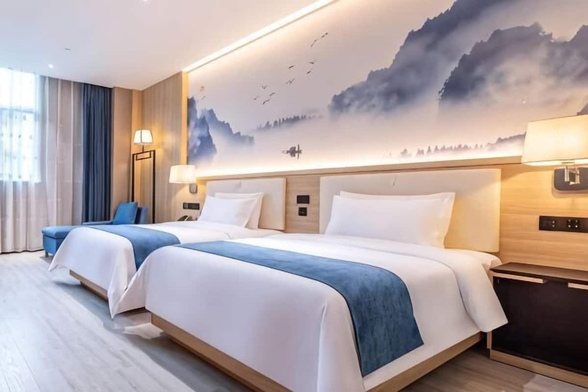 A hotel room with two beds, a large wall mural, a desk, and a chair.