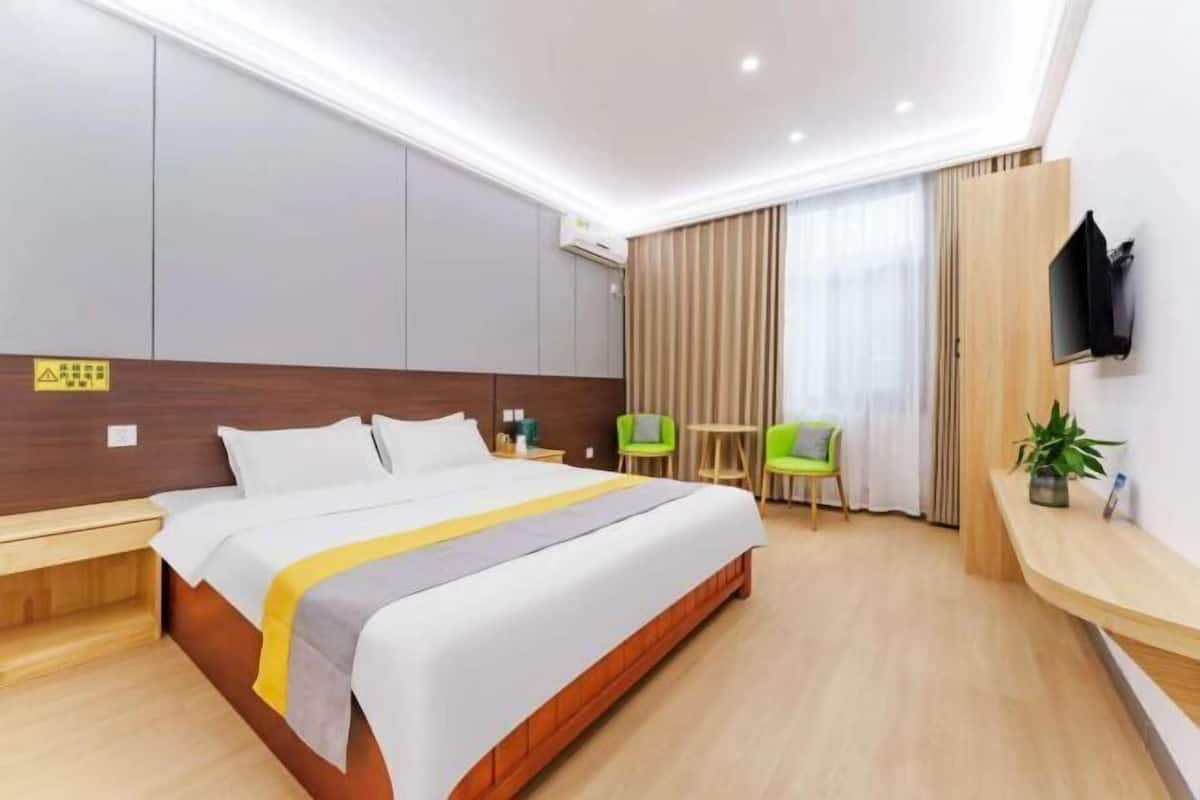 A hotel room with a large bed, bedside tables, a TV, a small table, two chairs, and a potted plant.