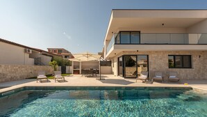 Ein modernes Haus mit Schwimmbad, Sitzgelegenheit im Freien und einer Steinsäule.