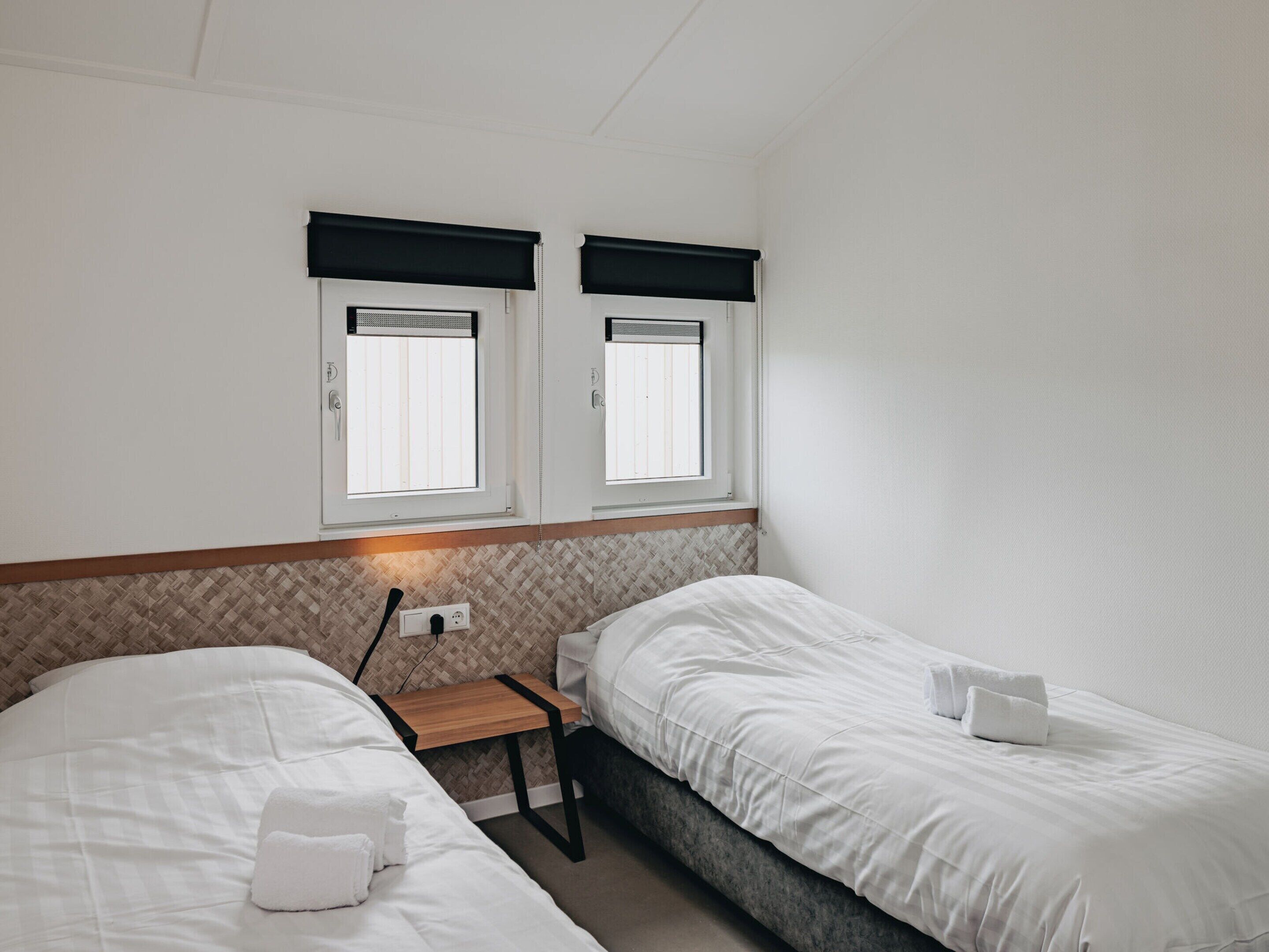 A bedroom with two beds, a nightstand, and a window with a black blind.