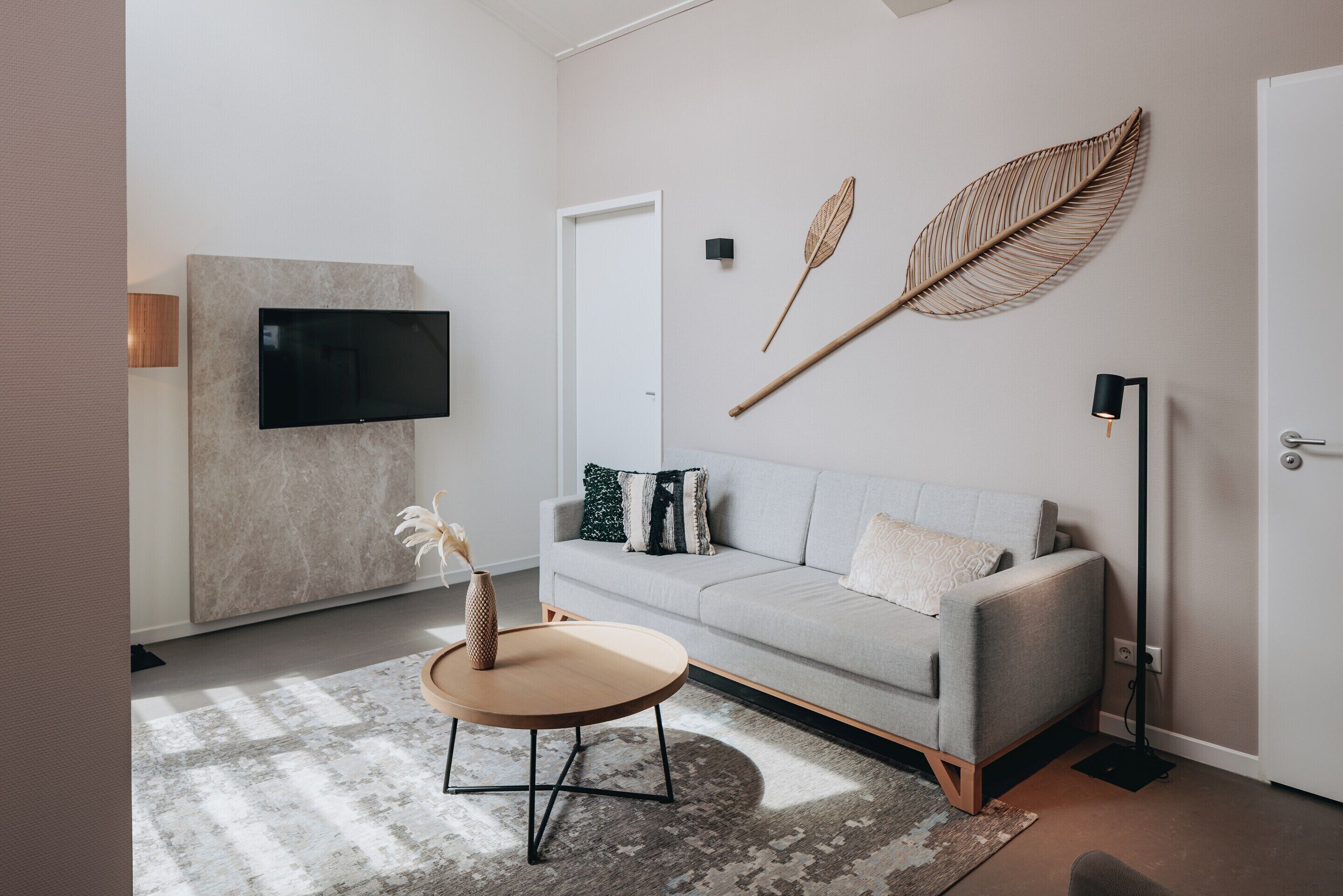 A modern living room with a grey sofa, a round coffee table, a mounted TV, and decorative wall art.