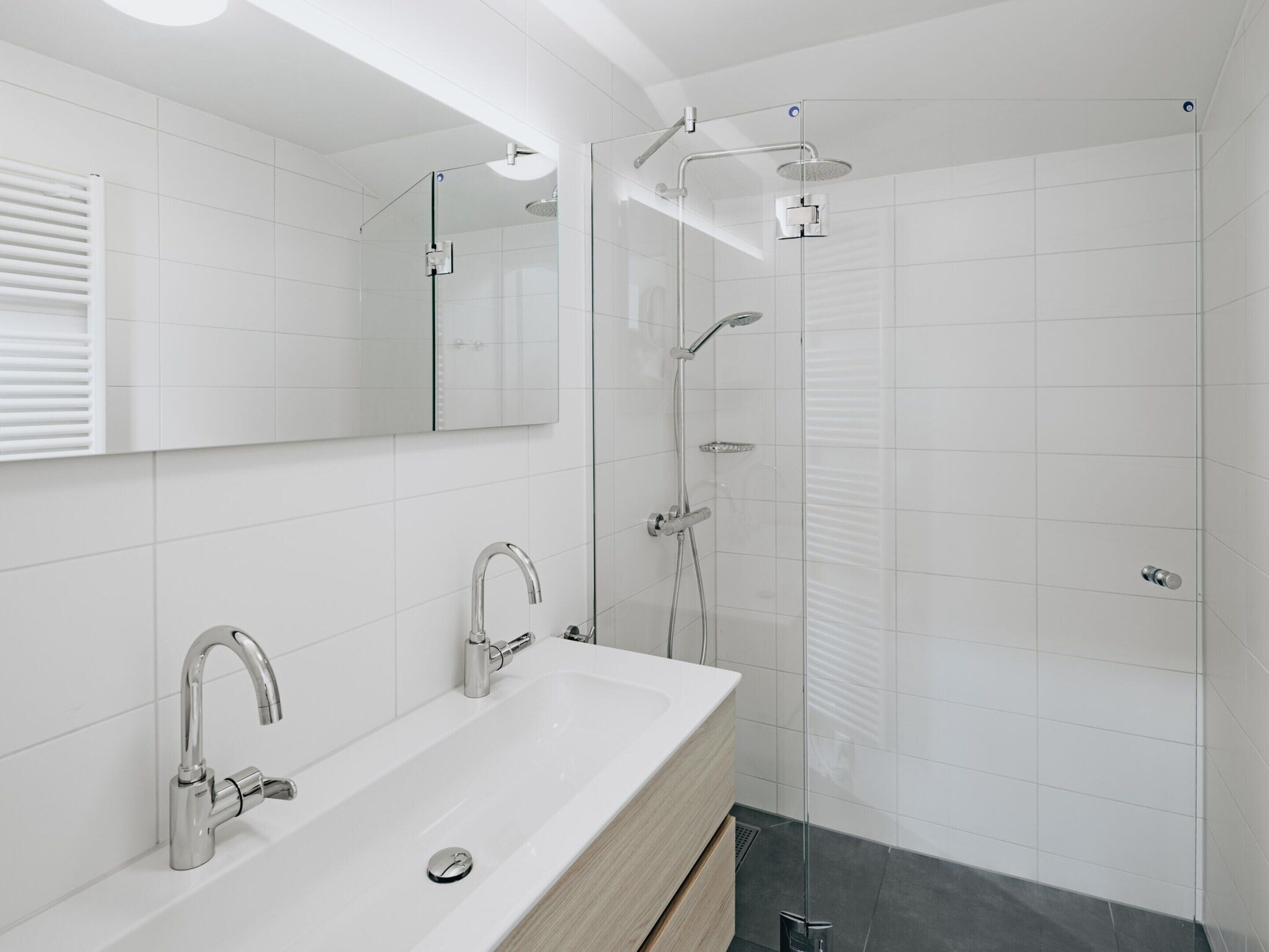 A modern bathroom with a large mirror, a sink with two faucets, and a glass-enclosed shower area.