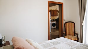 A bedroom with a bed, a chair, and a view into a laundry room. - Maison Cosy I Terrasse Privée (Nemours)