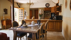 A kitchen with wooden cabinets, a dining table with chairs, a chandelier, and a clock on the wall. - Maison Cosy I Terrasse Privée (Nemours)
