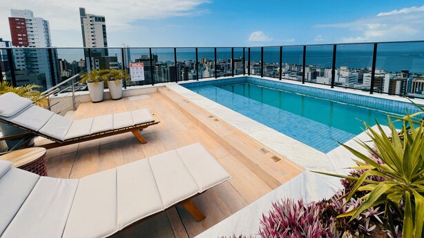 Ein Pool auf dem Dach mit Liegestühlen und Topfpflanzen mit Blick auf Stadt und Meer.