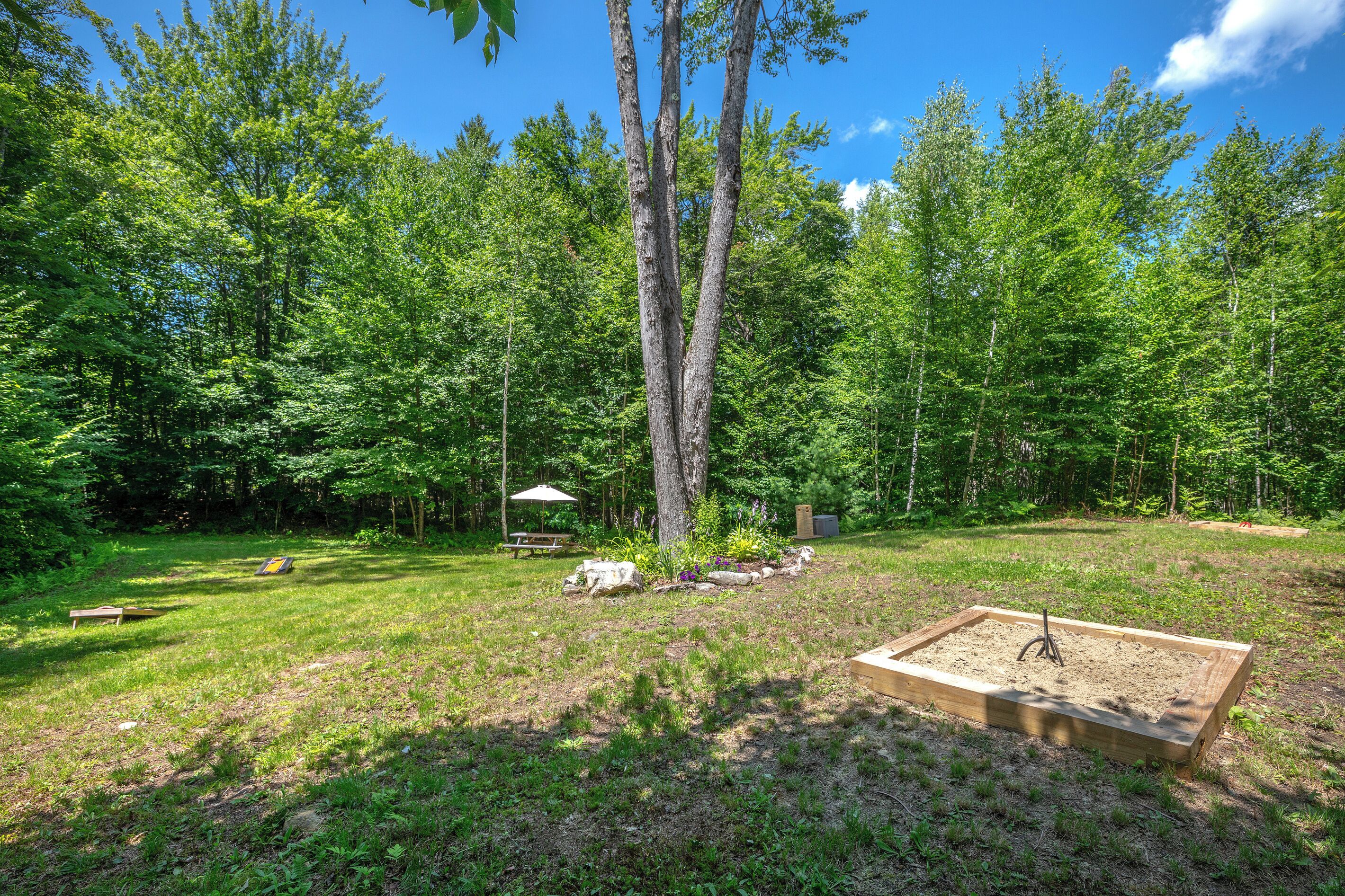 Ein Garten mit Bäumen, einer Holzterrasse, einem Picknicktisch und einer Bank.