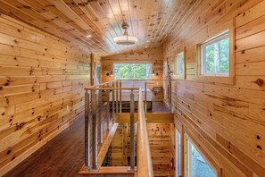Interieur van een houten chalet met een centrale trap, houten wanden en een raam met uitzicht op de natuur.