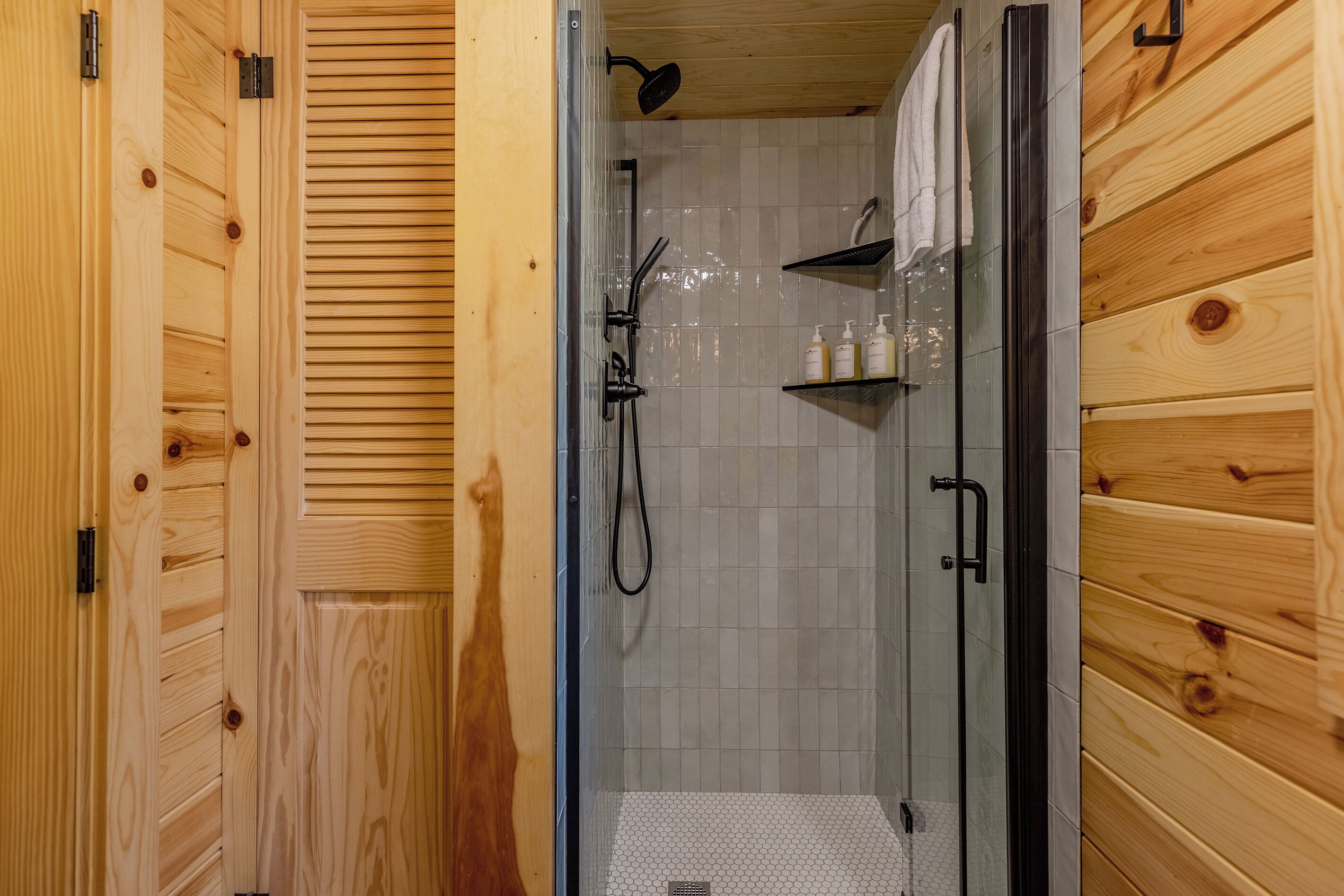 Interior de madera con zona de ducha empotrada en cristal, una toalla colgada en la pared y un estante con artículos de aseo.