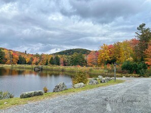 Un lago con un puente de madera, rodeado de árboles de colores otoñales y un paisaje montañoso.