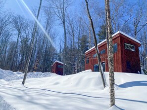 Una cabaña de madera con fachada roja, rodeada de nieve y árboles.