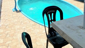 Une piscine avec une terrasse carrelée, un barbecue et une table avec des chaises.