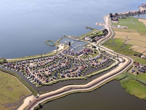 An aerial view of a lakeside residential area with houses arranged in a semi-circular pattern around a central park, connected by narrow roads.