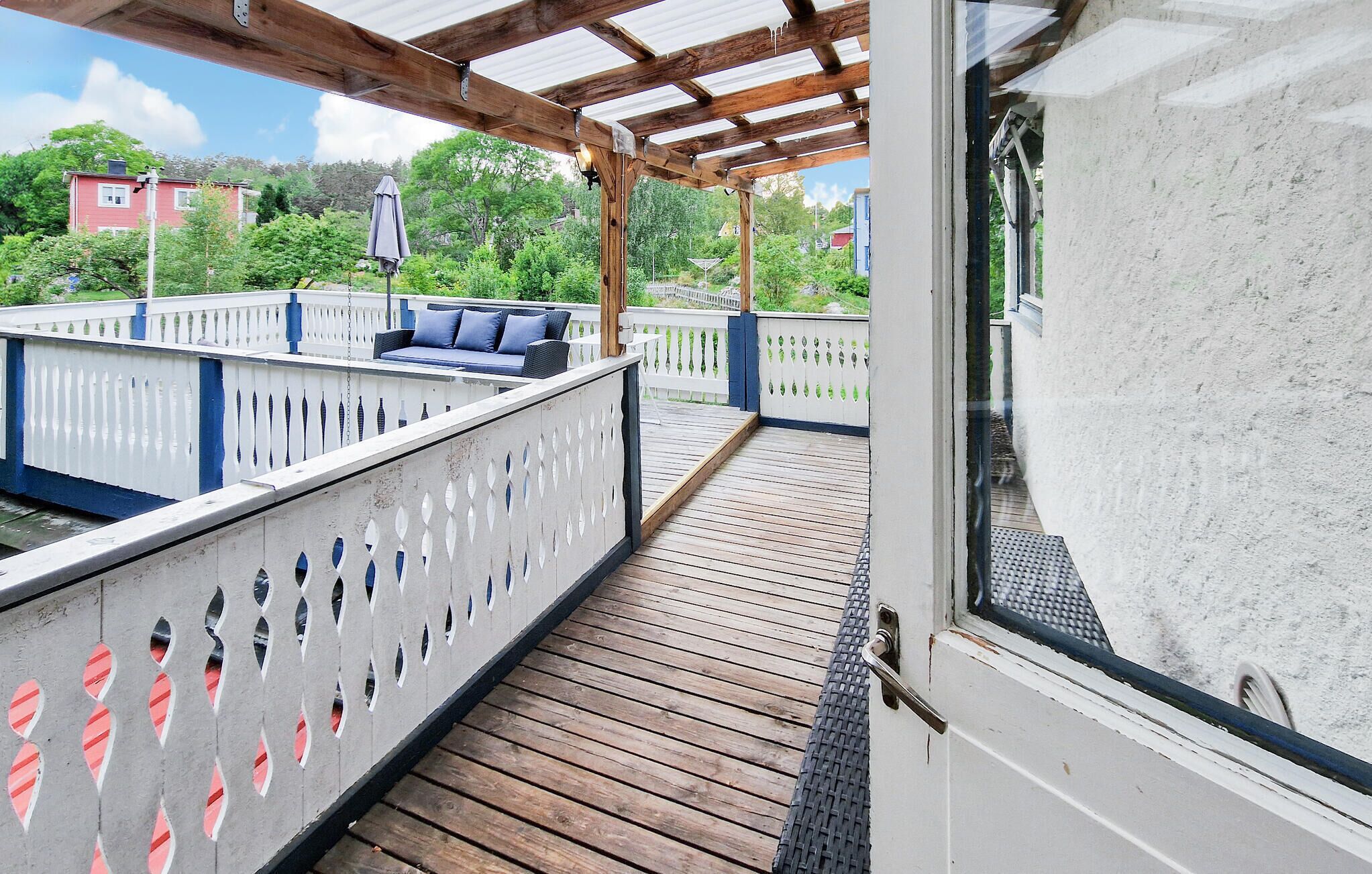 Una terraza techada con piso de madera, barandas blancas con detalles decorativos y un sofá azul.