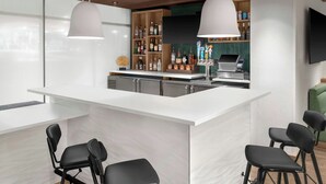 A modern bar area with a white countertop, black bar stools, and pendant lighting. -  Fairfield Inn & Suites by Marriott® Norwalk Des Moines (Norwalk)