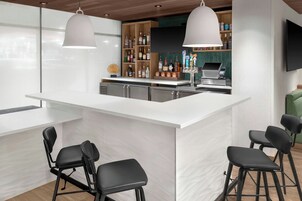 Zona de bar moderna con mostrador blanco, taburetes negros e iluminación colgante.