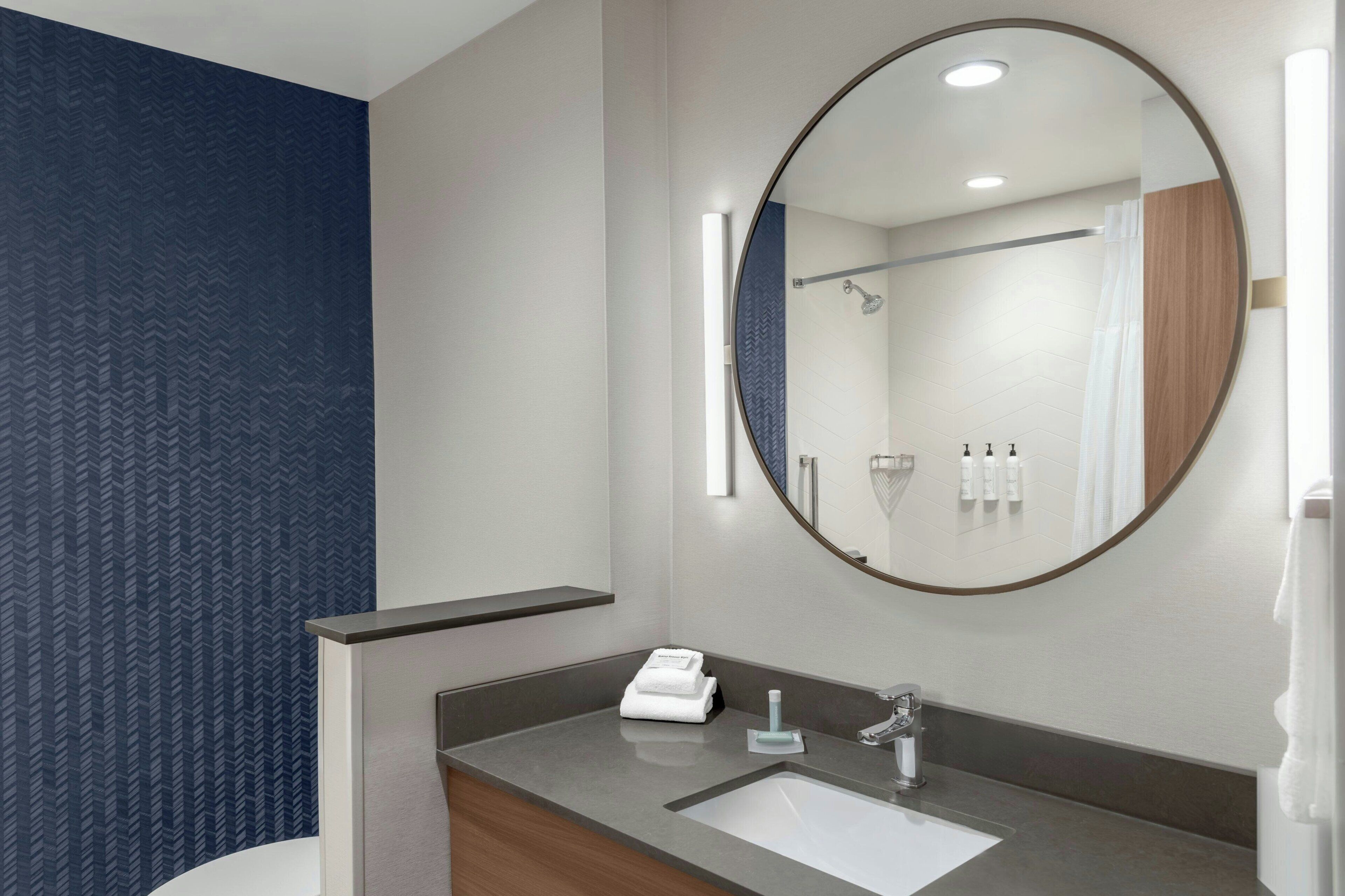 Un baño moderno con un espejo redondo grande, un lavamanos y una zona de ducha.
