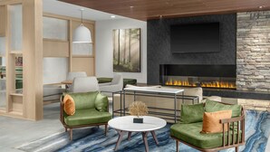 A modern living room with a fireplace, green upholstered chairs, a round coffee table, and a large painting on the wall. -  Fairfield Inn & Suites by Marriott® Norwalk Des Moines (Norwalk)