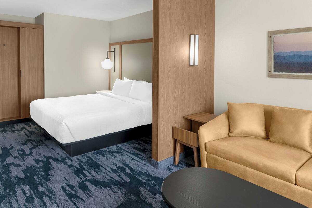 Una habitación de hotel con cama, sofá, escritorio e iluminación en la pared.