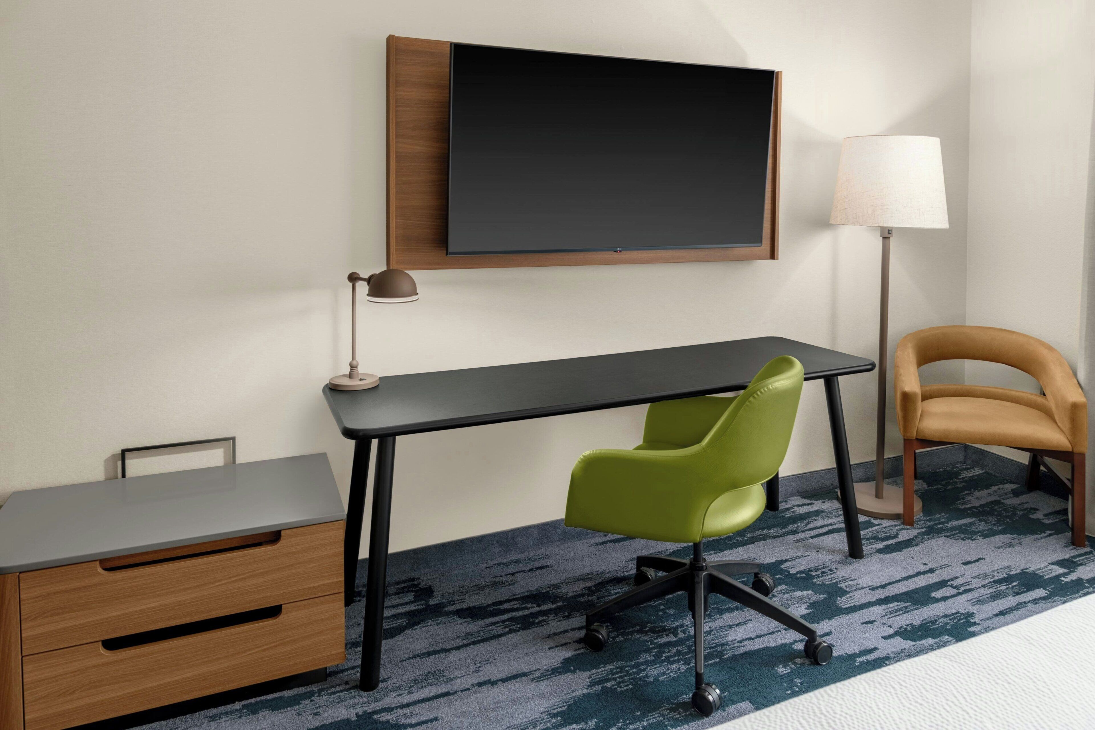 Ein Hotelzimmer mit Schreibtisch, einem grünen Sessel, einer Lampe und einem Bett.