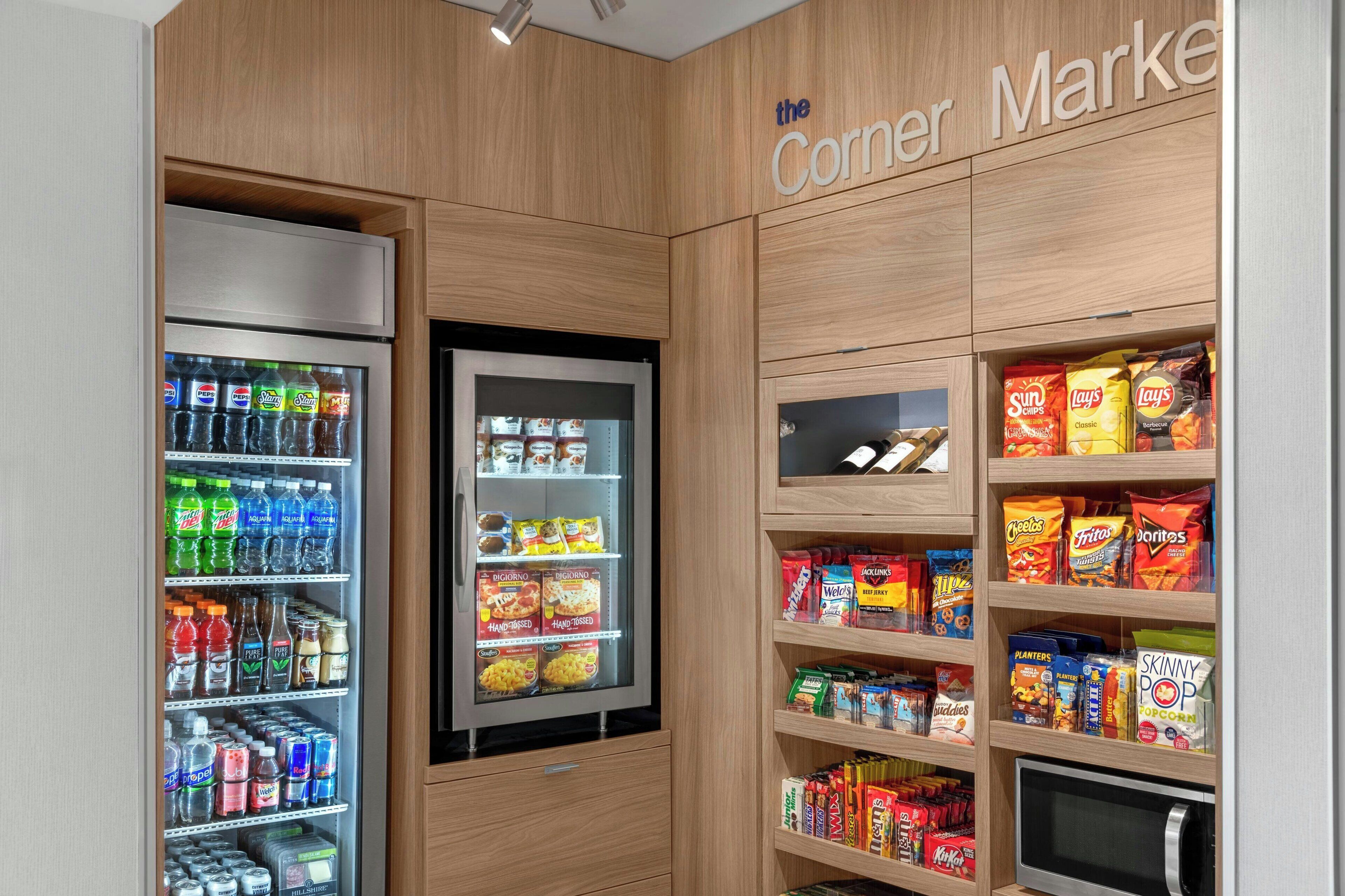 A corner store with a refrigerated beverage cooler, snack shelves, and a microwave.