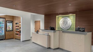 A reception area with a wooden reception desk, a vending machine, and a decorative wall piece. -  Fairfield Inn & Suites by Marriott® Norwalk Des Moines (Norwalk)