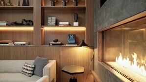 Una sala de estar moderna con chimenea, estanterías de madera con libros y adornos, un sofá con cojines y una lámpara de pie.