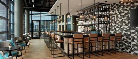 A modern bar area with a long counter, bar stools, and a geometric patterned wall.