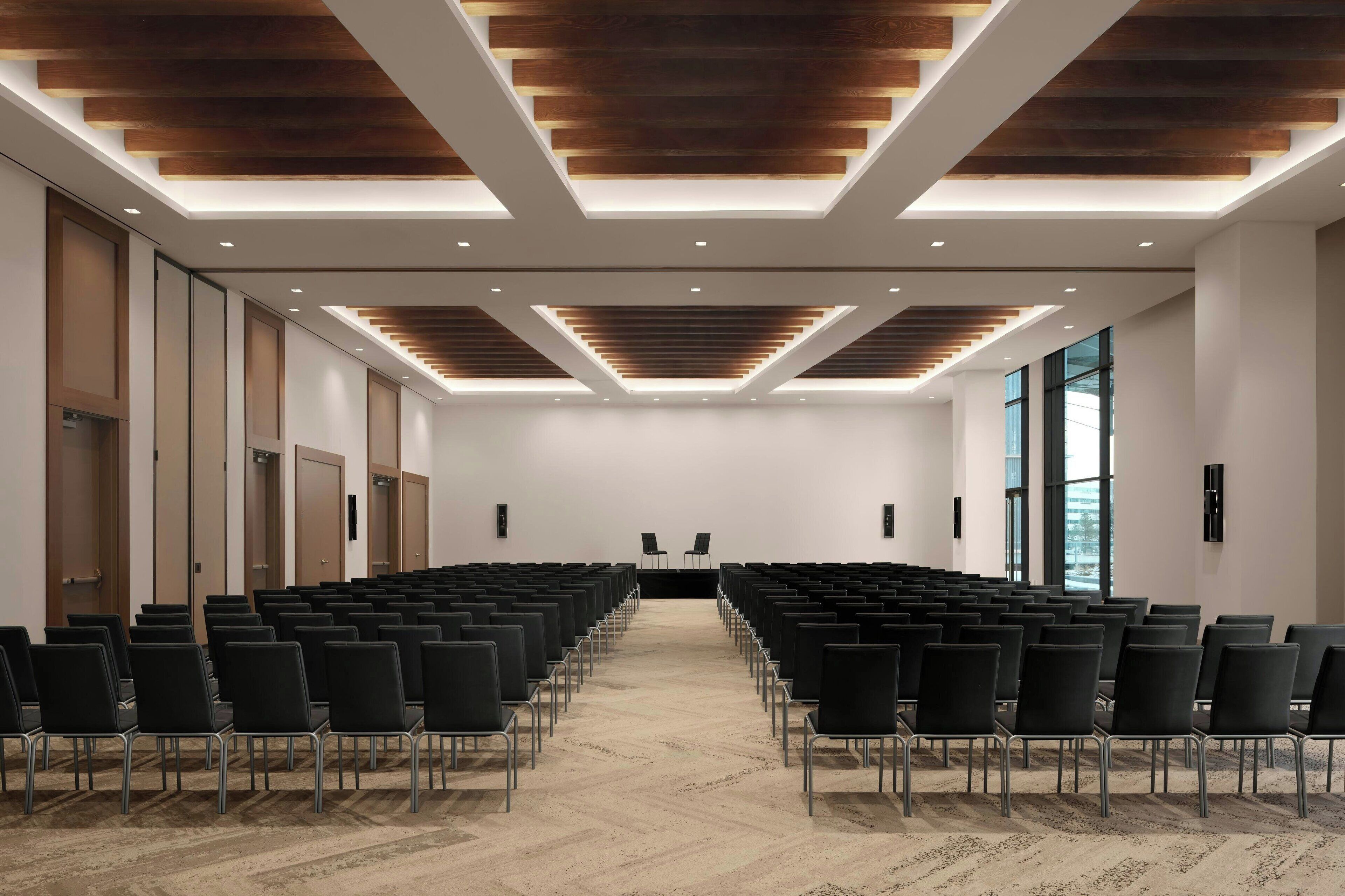 A conference room with rows of chairs, a stage, and a modern ceiling design.