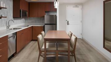 A modern kitchen with wooden cabinets, stainless steel appliances, a dining table with chairs, and a pendant light.