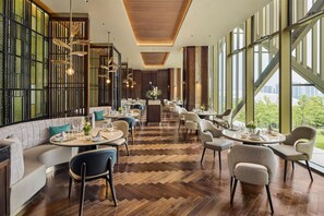 A modern dining area with multiple tables and chairs, large windows, and a herringbone wood floor. - Chongqing Lijia Baiyun Lake Hotel, Curio Collection Hilton (Chongqing)