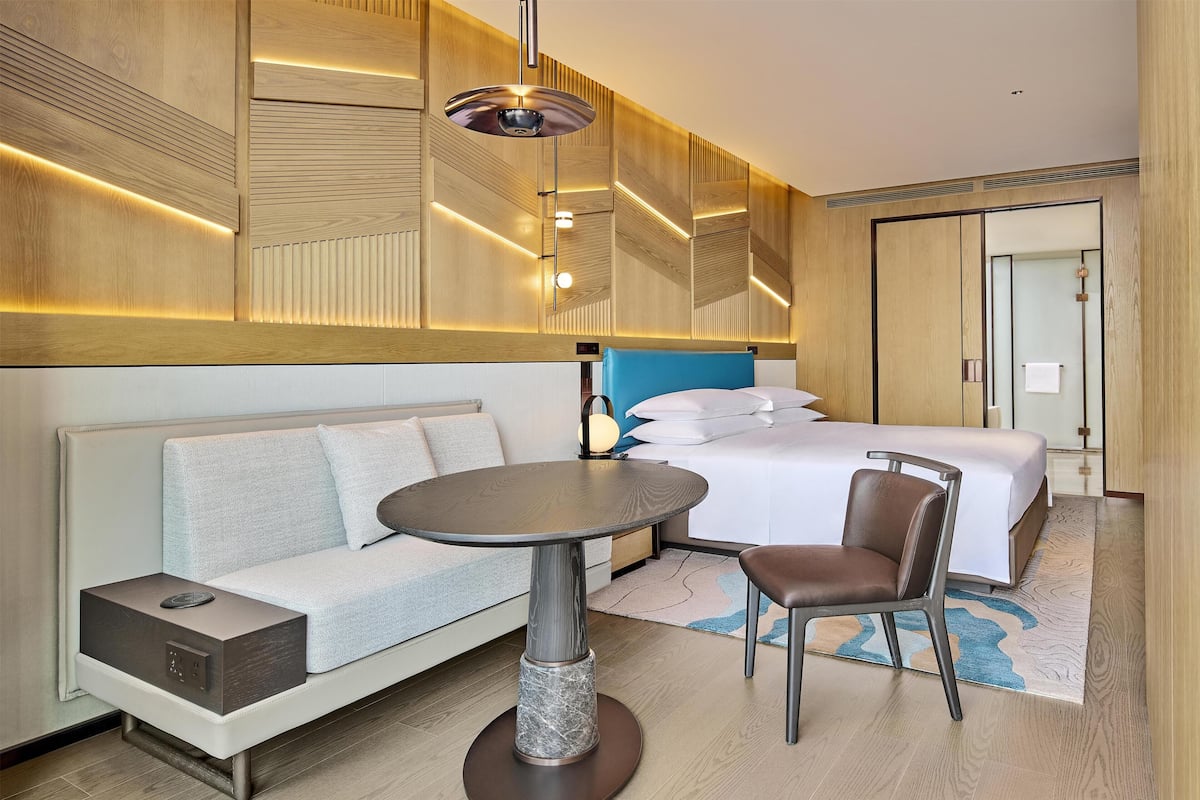 A modern hotel room with a bed, sofa, dining table, and a chair.