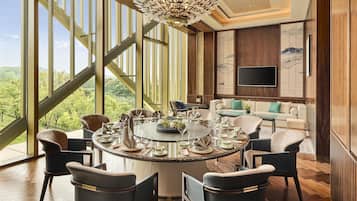 Comedor con una mesa redonda dispuesta para seis personas, rodeada de sillas, y vistas a zonas verdes a través de grandes ventanales.