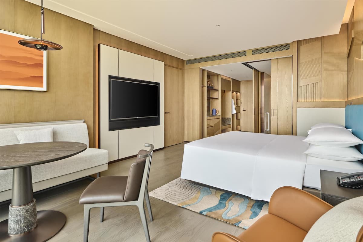 A hotel room with a bed, a TV, a sofa, a dining table, and a chair.