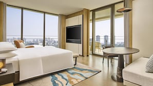 Ein Hotelzimmer mit einem großen Bett, einem Fernseher, einem Esstisch und einem Balkon mit Blick auf die Stadt.