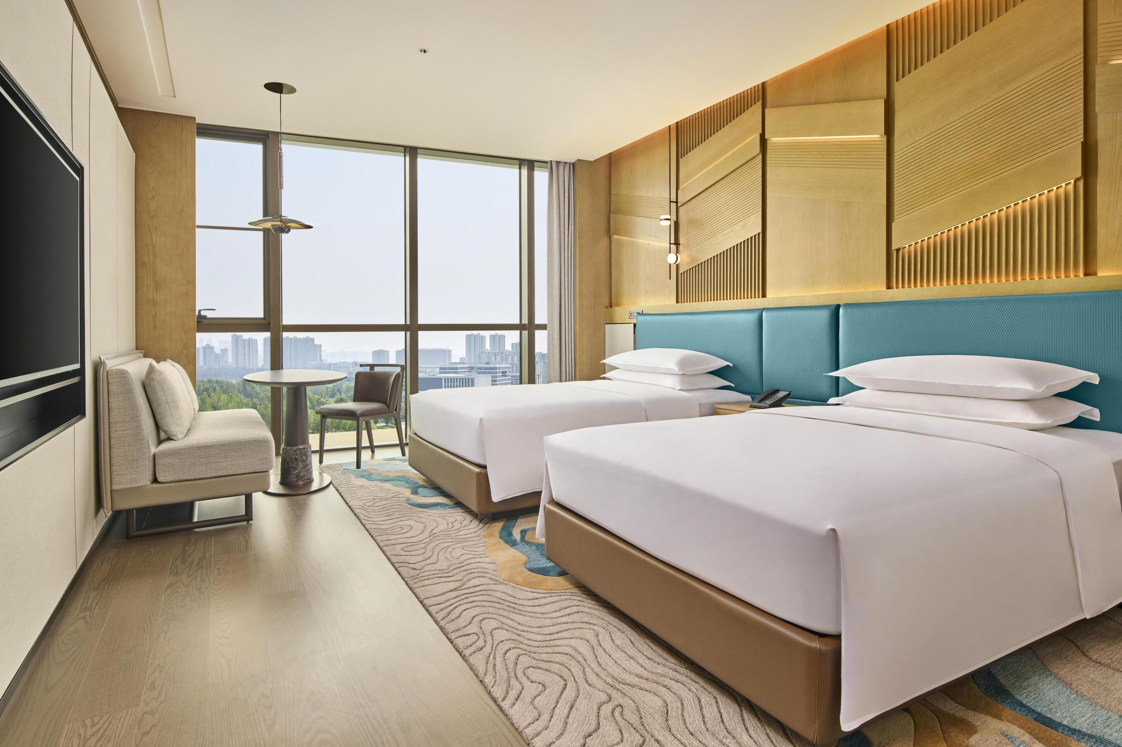 A hotel room with two beds, a sofa, a small table, and a city view.