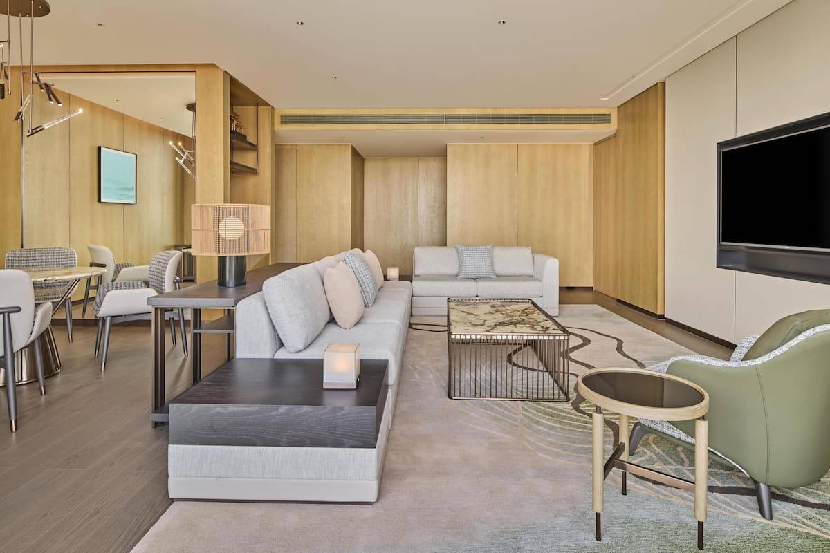 A modern living room with a sofa, coffee table, and chairs, a television, and a dining area with a table and chairs.