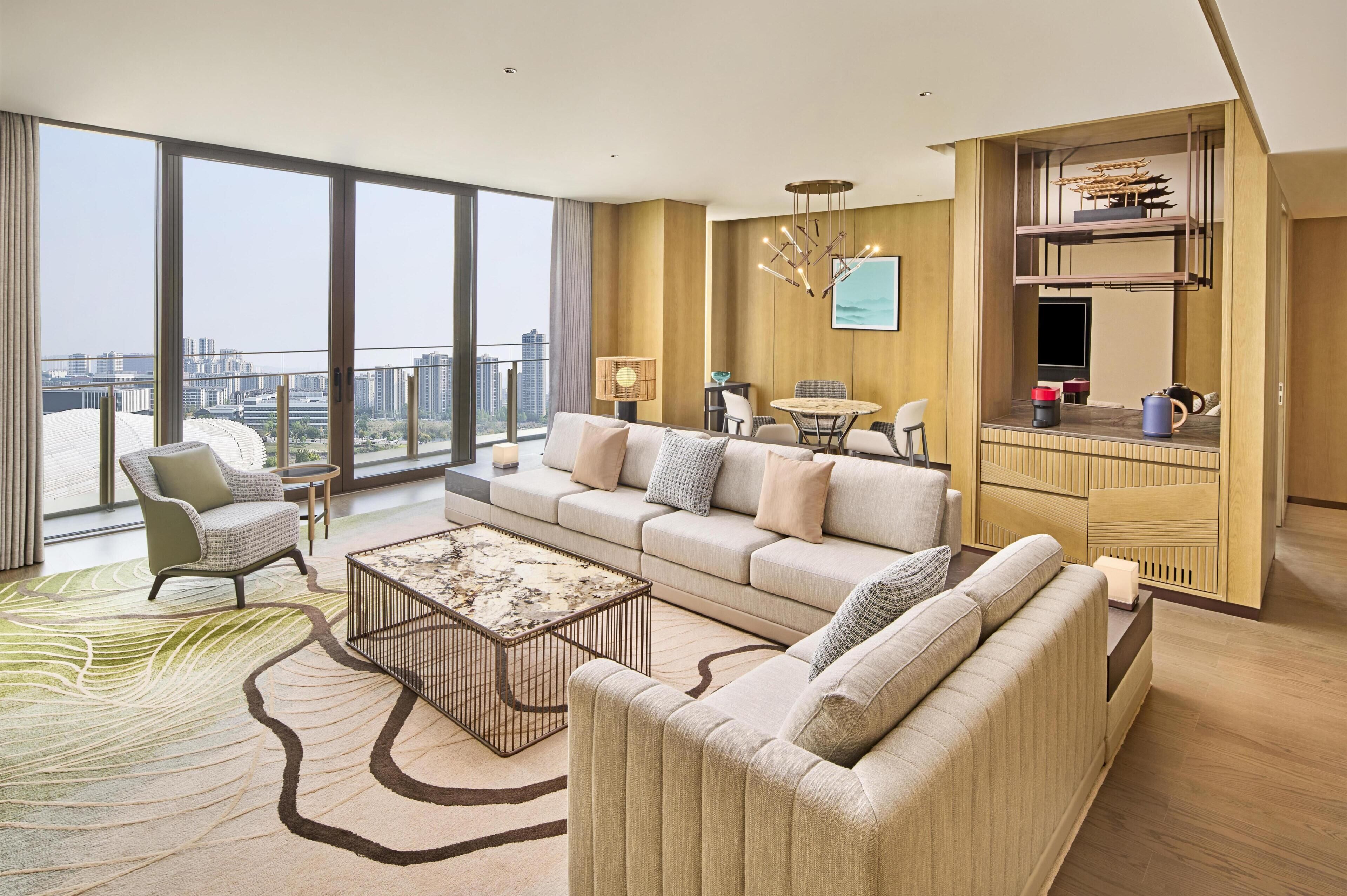 A modern living room with a sofa, armchair, coffee table, and a dining area with a table and chairs.
