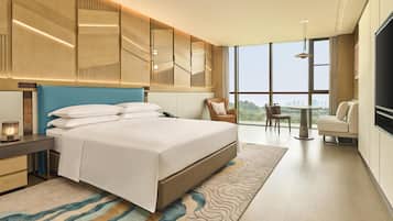 Quarto de hotel moderno com uma cama grande, uma escrivaninha, uma cadeira, uma televisão e vista para a cidade.